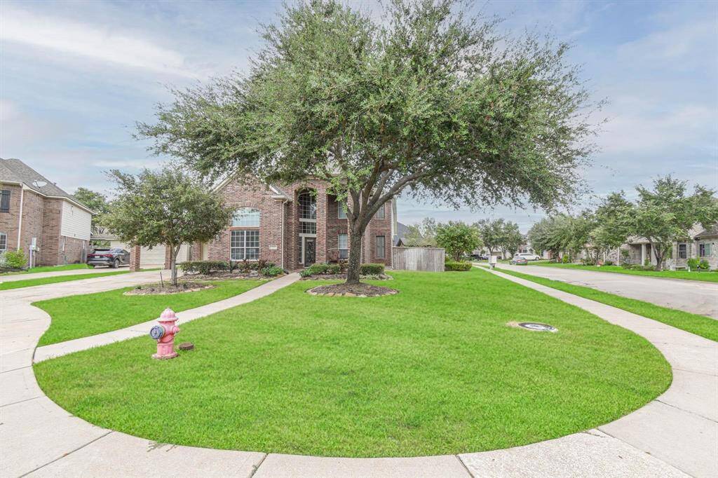 This photo showcases a charming brick home on a spacious corner lot with a well-maintained lawn and mature trees. The property features a curved driveway and a neighborhood setting, offering a welcoming curb appeal.