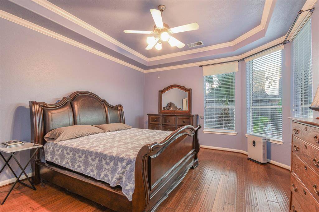 Spacious primary bedroom featuring elegant tray ceilings, abundant natural light, and warm hardwood floors.