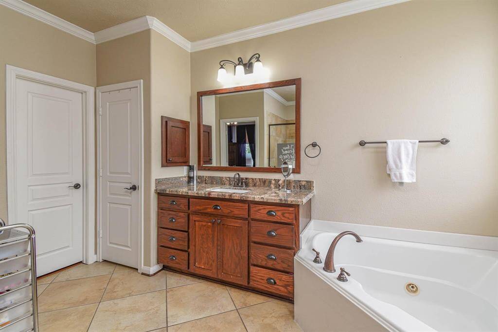 Elegant primary bathroom featuring a luxurious soaking tub, spacious vanity with rich wood cabinetry, and sleek tile flooring for a serene retreat.