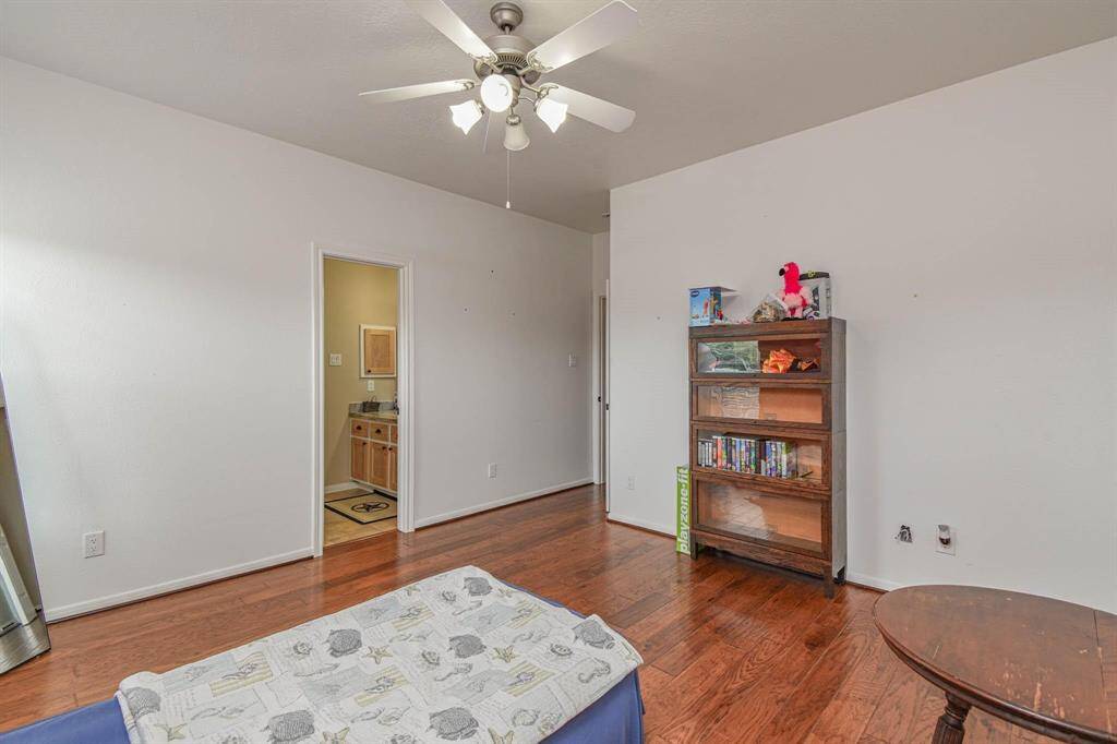 This room features hardwood floors, a ceiling fan, and neutral walls. It includes a doorway leading to another area, likely a bathroom or closet, and has a wooden bookcase for storage.