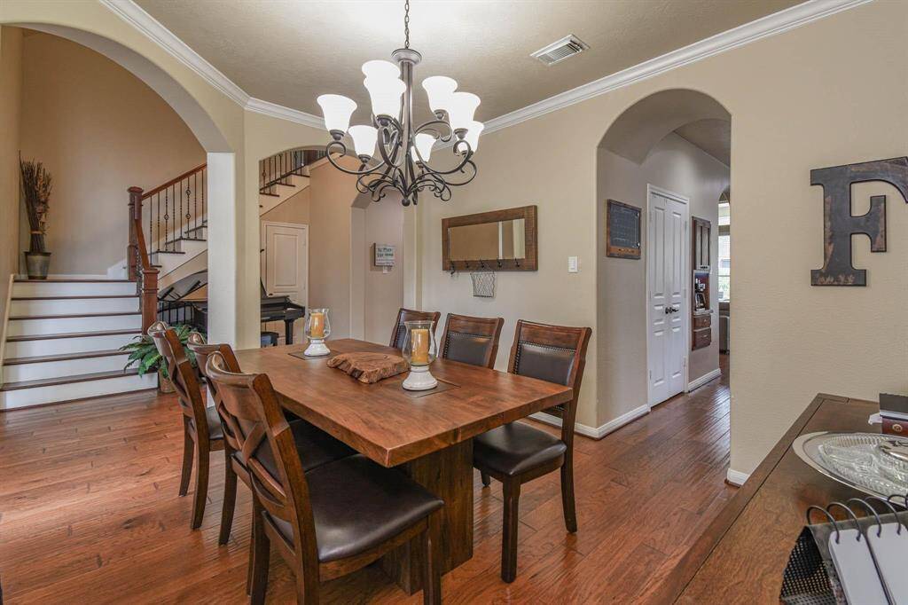This inviting dining area features warm hardwood floors and an elegant chandelier. It opens to a staircase with charming wood and iron details, leading to additional living spaces. The room is accented with archways and neutral tones, creating a cozy atmosphere.