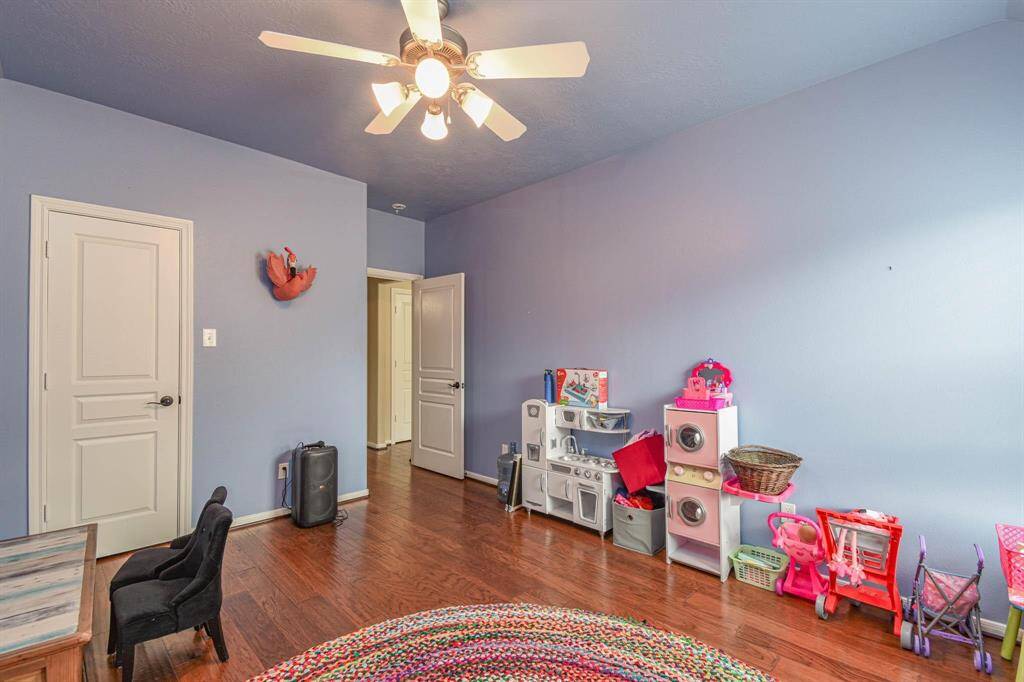 This photo showcases a cozy room with hardwood floors and light blue walls, ideal for a child's playroom. It features a ceiling fan, built-in storage, and colorful children's toys. The room has a modern, clean feel with white doors and ample natural light.