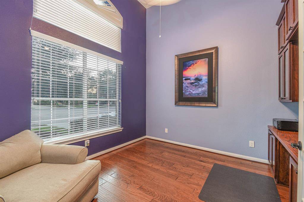 This room features a large window offering natural light. It has hardwood floors, a cozy armchair, and built-in wooden cabinets. A large framed artwork adds a decorative touch.