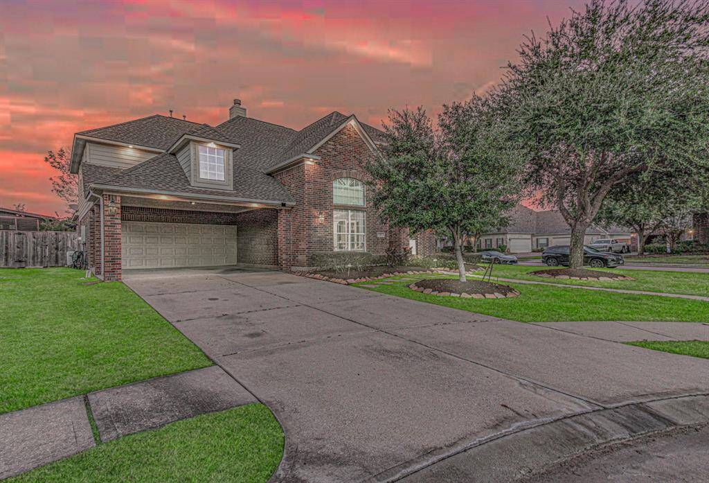 This beautiful two-story brick home features a spacious driveway leading to a two-car garage. The well-maintained front yard is adorned with mature trees and neat landscaping. The house sits in a tranquil neighborhood, offering a serene setting against a picturesque sunset sky.