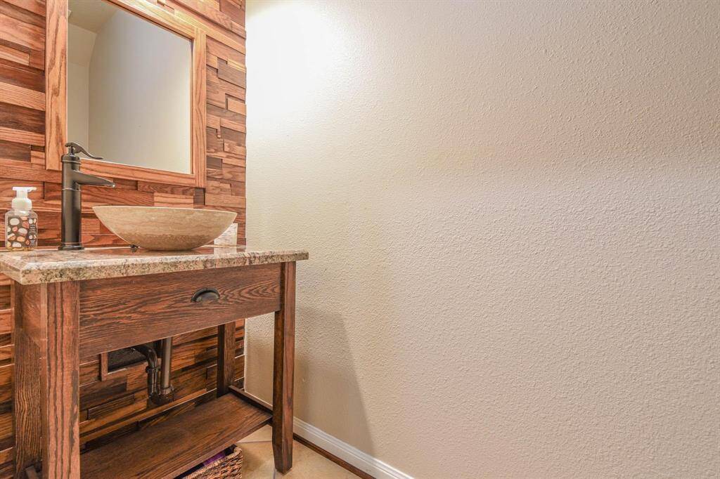 This photo shows a stylish bathroom with a rustic wooden vanity, a modern vessel sink, and a sleek black faucet. The wall features a textured wood panel accent, contrasting with the neutral paint, creating a warm, inviting atmosphere.