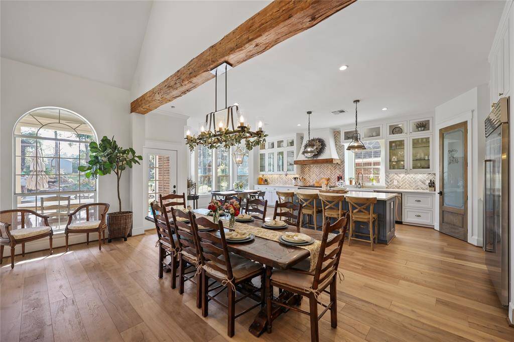 A beautifully designed dining and kitchen area with a warm, inviting atmosphere. The natural light floods the room through large windows and a glass-paneled door leading to an outdoor area