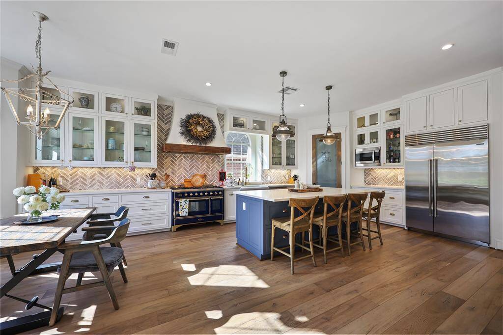 This kitchen is a perfect combination of elegance, and practicality, designed for both everyday life and entertaining. The paver herringbone-patterned backsplash creates texture, while the custom vent hood compliments the large gas range.  Glass-front custom cabinets provide a mix of storage and display opportunities, and  the custom built pantry and door, with its frosted glass detailing, adds a vintage touch. The Sub-Zero stainless steel refrigerator balances the classic elements with modern convenience.