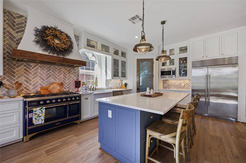 A stunning, light-filled kitchen and breakfast nook, beautifully remodeled in January '22. This thoughtfully designed space features a custom oversized island with a rich dark base, creating a striking contrast against the white custom cabinetry and light quartz countertops. All appliances were replaced in January 2022, with the highlight being a luxury Italian cooking range paired with a custom vent hood. The neutral-toned herringbone backsplash adds texture and depth, elevating the atmosphere.