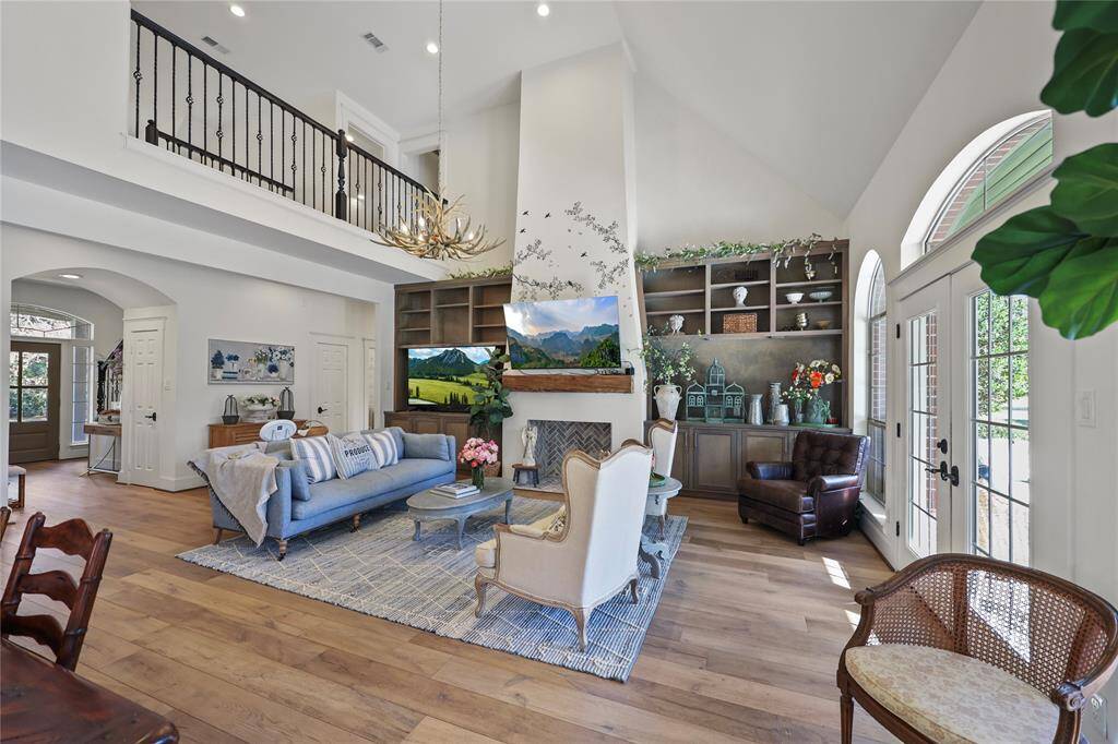 The high ceilings, natural lighting, and warm wood flooring create an inviting atmosphere of this beautifully designed living room. The faux fireplace and mantle serves as a striking focal point to add your own decorative elements. The combination of modern and traditional, along with the neutral color palette, enhances the elegant yet comfortable feel of the space.