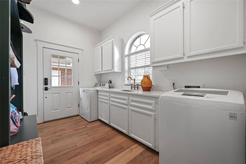 The laundry room features crisp white cabinetry, elegant quartz countertops, and a deep utility sink with a stylish brass-tone faucet. Enjoy plenty of storage with upper and lower cabinets, along with a built-in mudroom section equipped with a bench for seating, for organizing shoes, bags, and outerwear. The back door provides easy access to the outdoors.