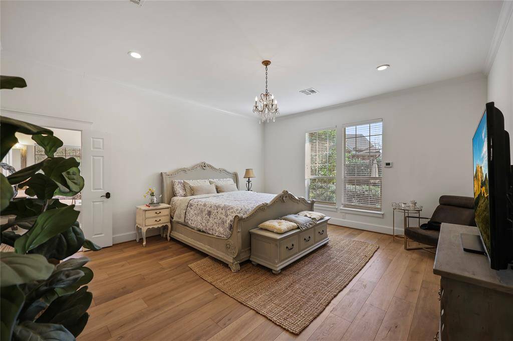 The primary bedroom features rich wood-look flooring, crisp white walls, and an abundance of natural light streaming through large windows with peaceful outdoor views