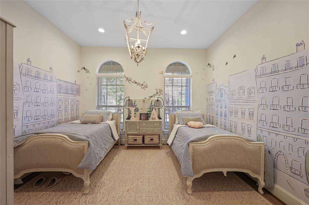 This secondary bedroom is located downstairs and has windows that overlook the expansive front yard, warm neutral tones and a beautiful chandelier light fixture.