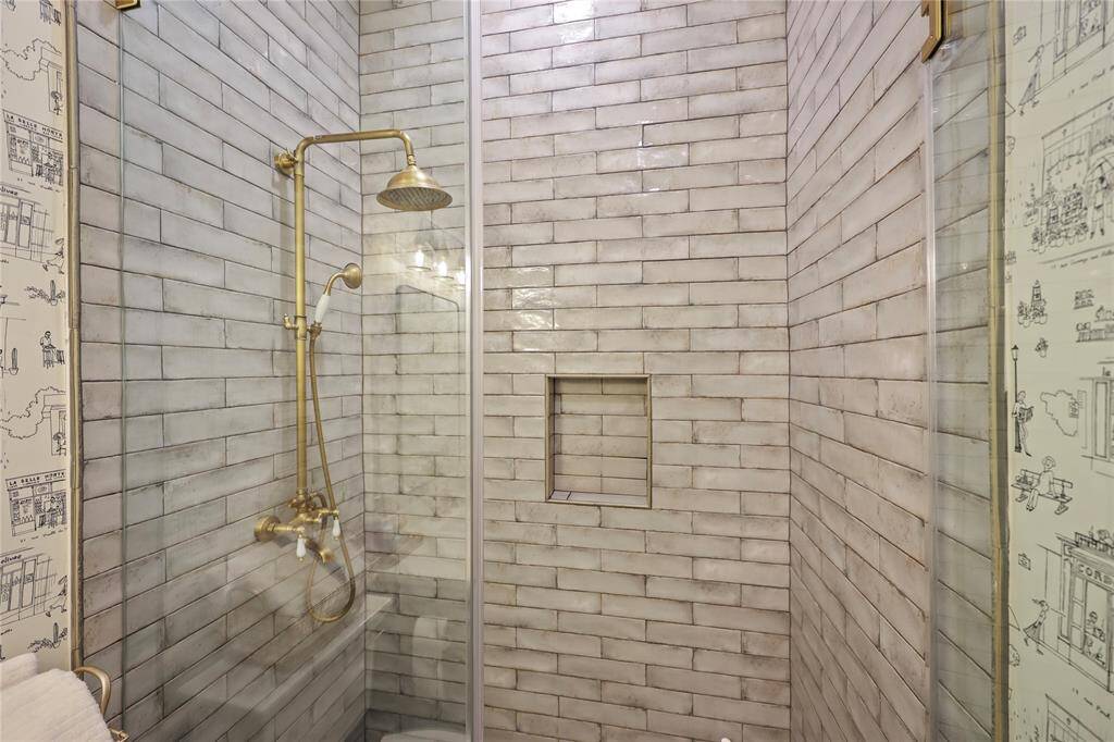 The glass enclosure shower with vintage-inspired subway tiles in a muted gray tone, complemented by elegant brass fixtures in the secondary bathroom.