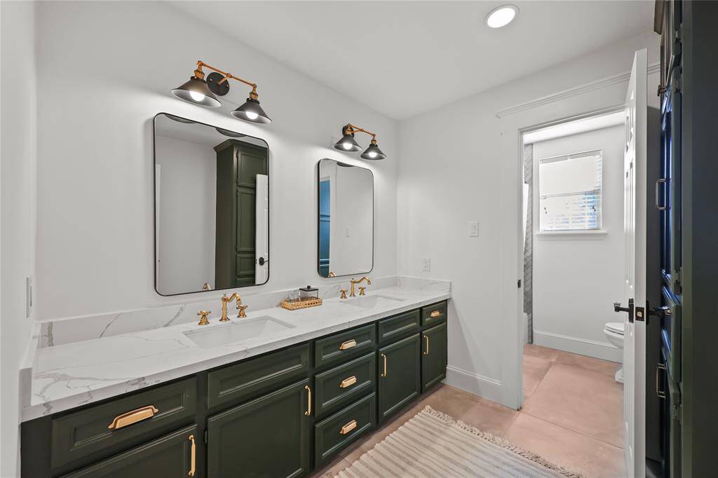 Another secondary bathroom  featuring a double vanity with dark cabinetry, gold hardware, and white quartz countertops. Two modern black-framed mirrors are complemented by modernl-style lighting. The space, with tile flooring, extends into a separate toilet and shower area.