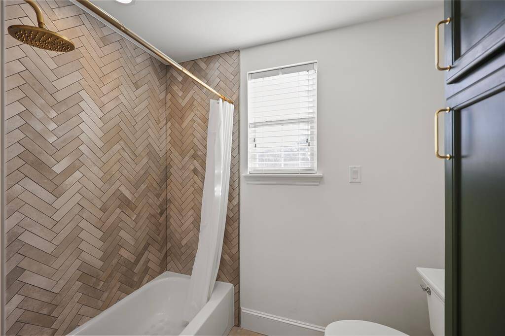 Recently remodeled shower/bathtub with a herringbone-patterned tile and a gold rainfall shower head.