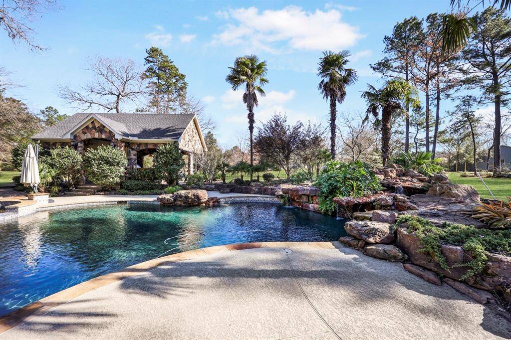 The resort-style pool with a rock waterfall, lush tropical landscaping, and tall palm trees. A stone pavilion houses an outdoor kitchen, half bath, and storage room and adds to the luxurye. The deck area beside the pool has room for lounge chairs to enjoy the sun after a splash in the pool.