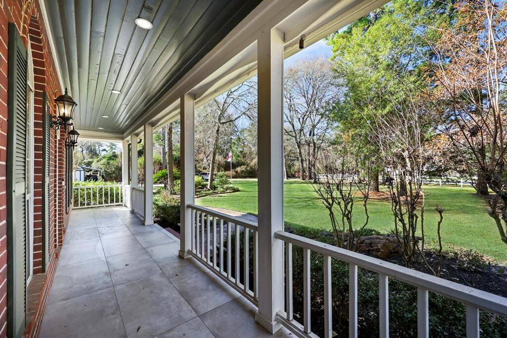 Classic black lantern-style wall sconces add a touch of traditional charm to this covered front porch The porch features elegant white railings and square columns, and overlooks the expansive front lawn.