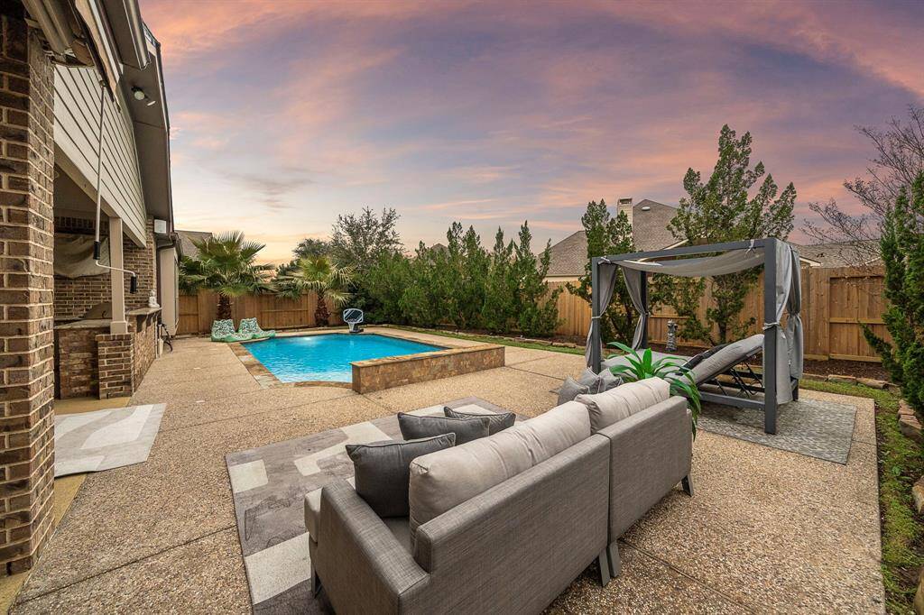 Outside, the lush backyard oasis creates a tropical paradise with mature landscaping providing a wall of privacy, a sparkling pool, and an outdoor kitchen—ideal for Texas summers.
