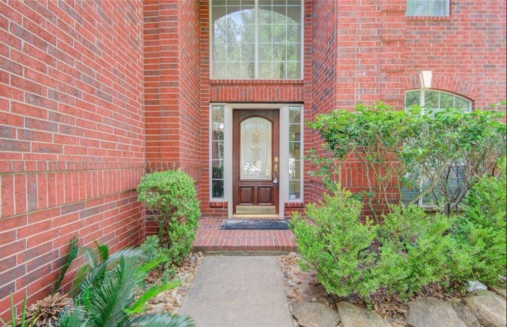 The rich red brick exterior complements the stately design, while the covered entryway provides a welcoming touch. Lush landscaping and a neatly paved walkway lead up to the door, enhancing the home's curb appeal.