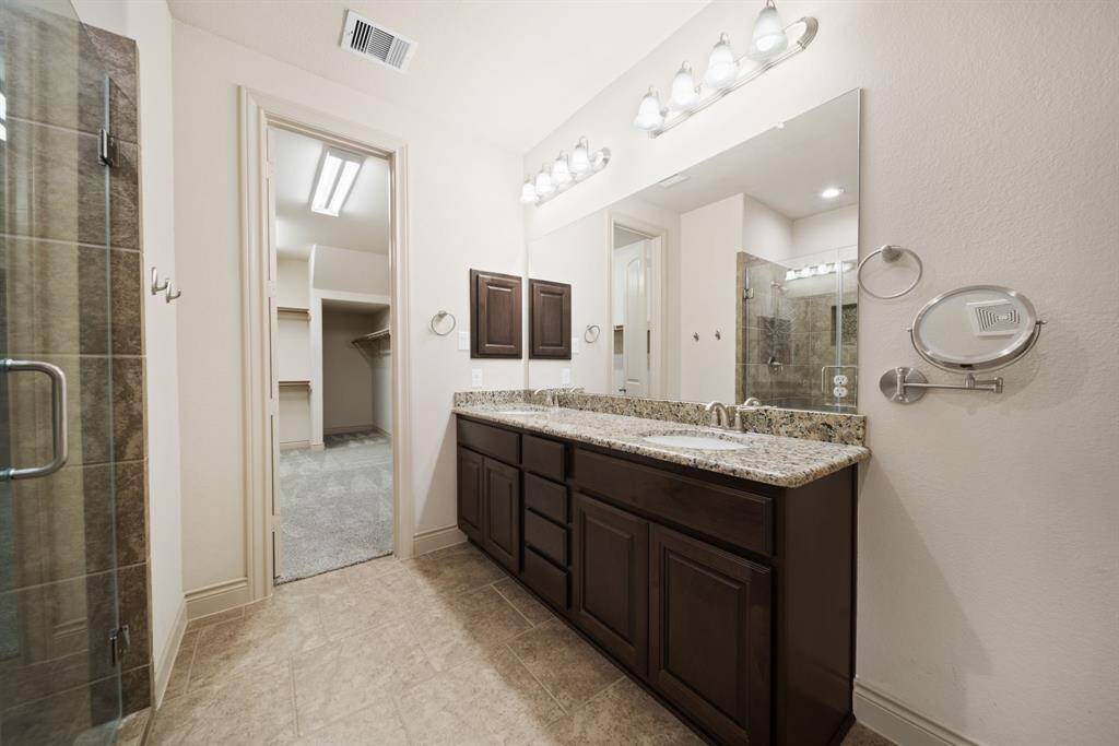 Primary bathroom with tile flooring, granite countertops, double sinks & a walk in closet w/ built-ins & easy access to the laundry room!