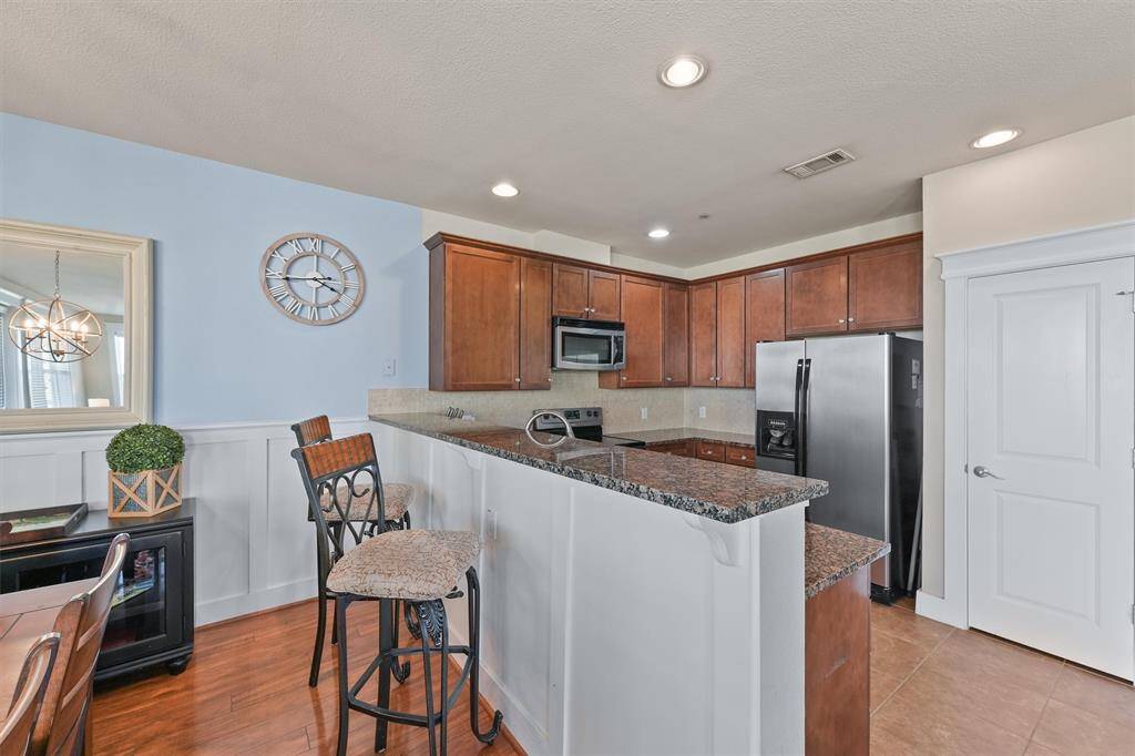 The kitchen features a raised breakfast bar with seating, perfect for casual dining or entertaining. The design includes warm wood cabinetry and sleek granite countertops, creating a modern and functional space.