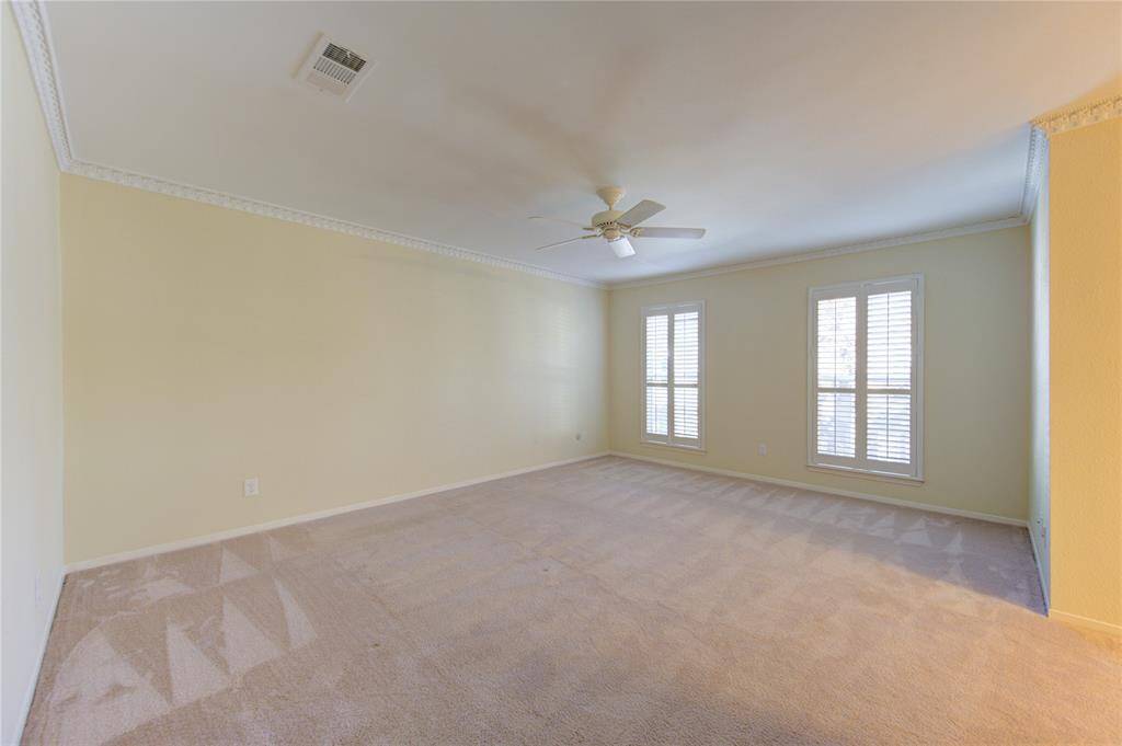 This spacious second bedroom features carpeted flooring, and large windows with shutters, offering plenty of natural light. A ceiling fan adds comfort to the space.