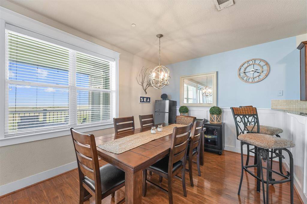 This view of the dining room showcases the ample natural light and the beautiful outdoor scenery visible through the large windows. The room's decor, including a modern chandelier and coastal-themed accents, creates a warm and inviting atmosphere.