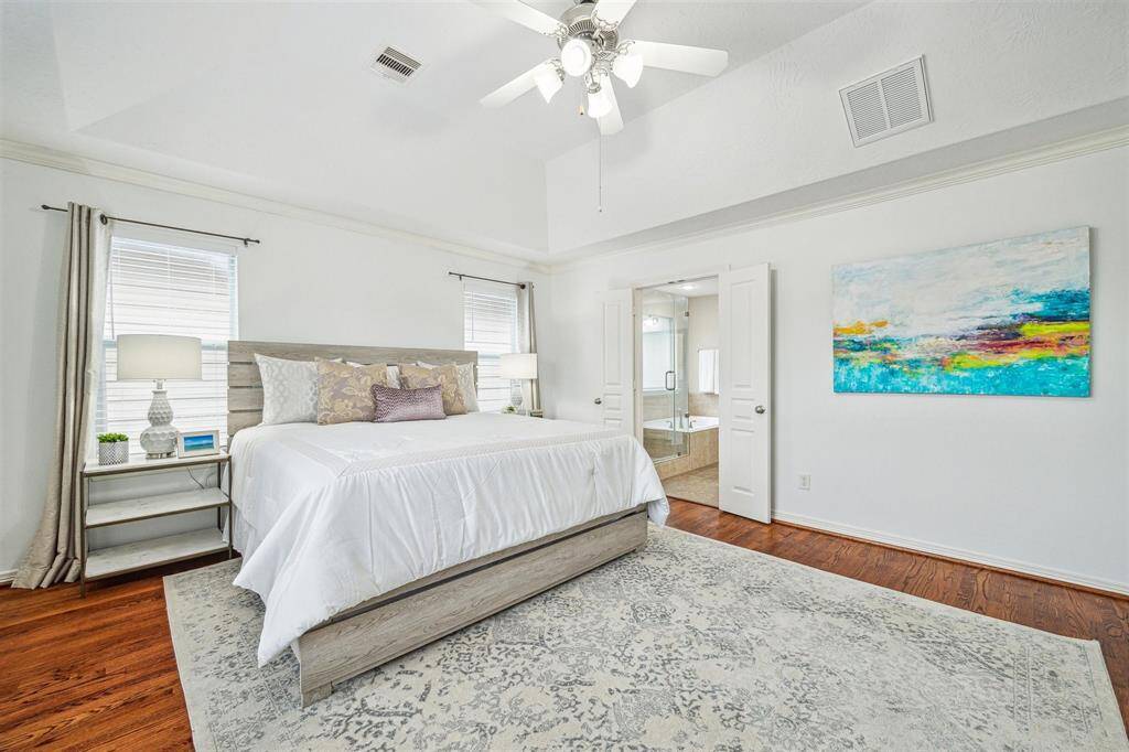 Primary bathroom with hardwood floors, vaulted ceiling and ceiling fan with lights.