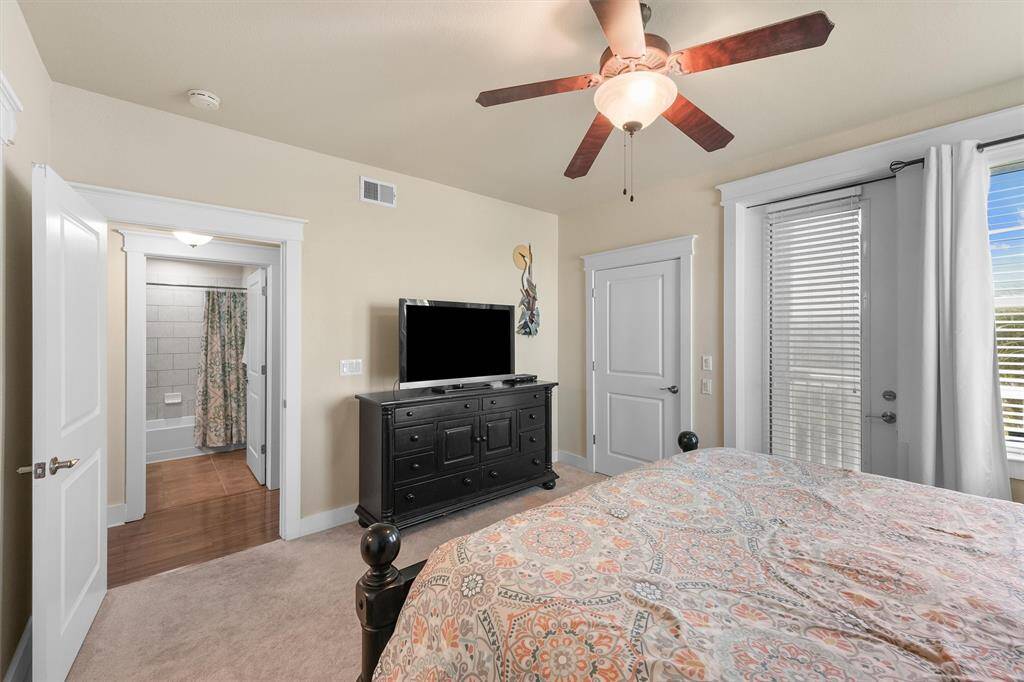 This angle of the primary bedroom highlights the comfortable king-sized bed and the direct access to both the walk-in closet and the private balcony. The room is equipped with a ceiling fan for added comfort and a TV for entertainment.