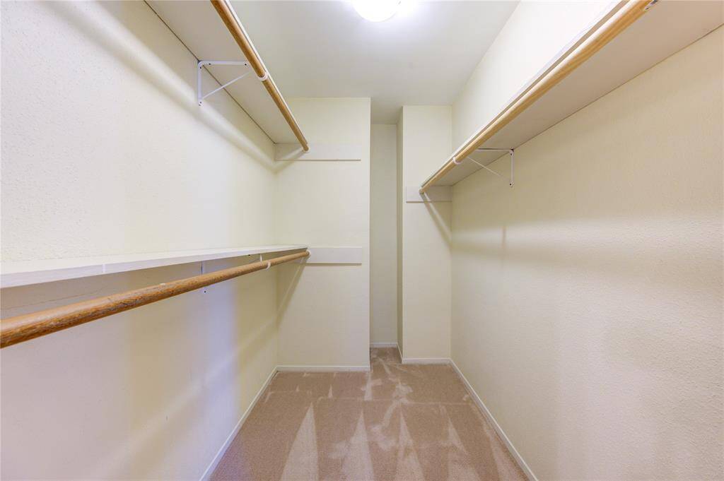 Spacious walk-in closet with ample shelving and hanging space in the primary bedroom, featuring neutral walls and carpet flooring.