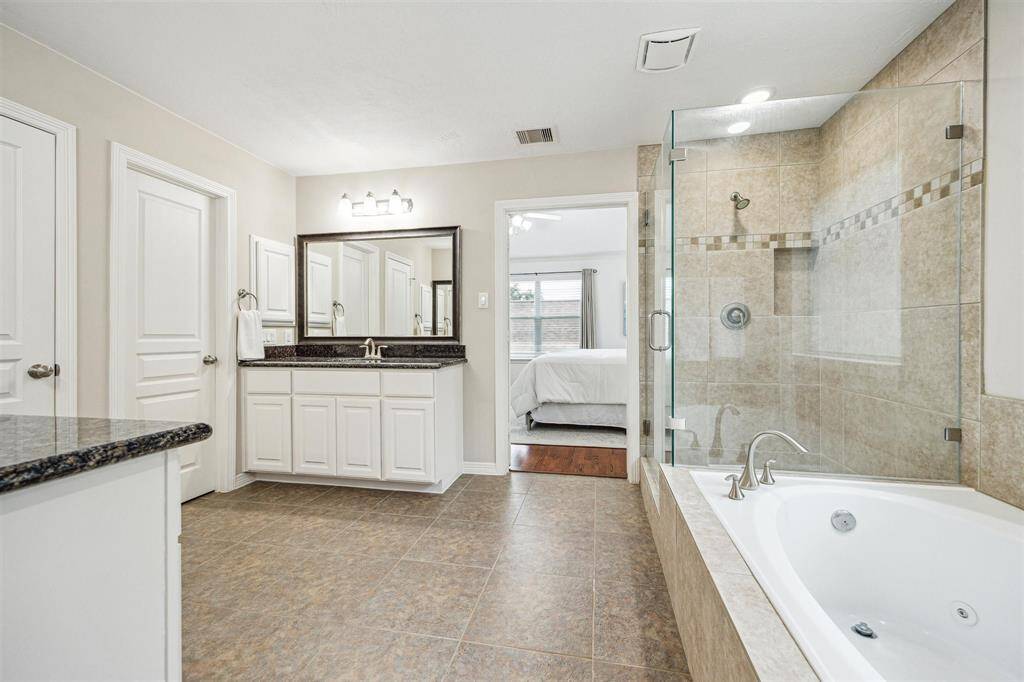 The primary bathroom features split vanities, a soaking tub, and a walk-in glass shower.