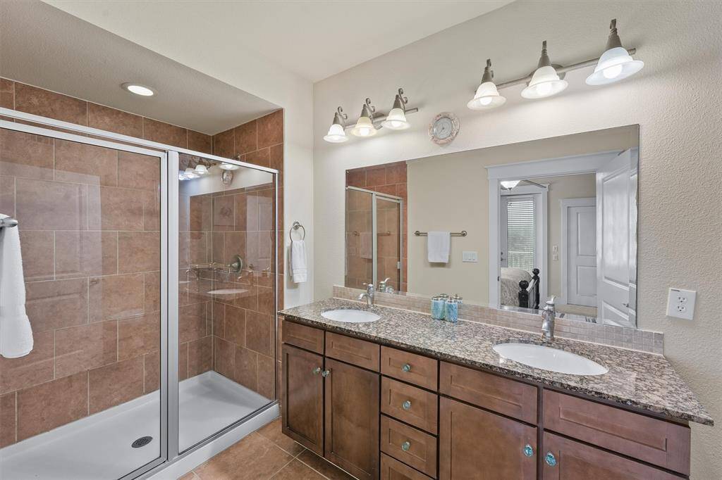 The primary bathroom features a spacious double vanity with granite countertops and ample storage. A large, glass-enclosed shower with elegant tilework adds a touch of luxury to the space, while bright lighting fixtures ensure a well-lit and inviting environment.