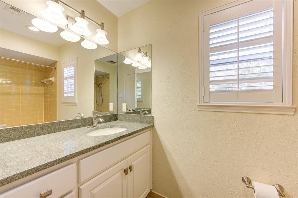 Spacious primary bathroom featuring sleek granite countertops, modern lighting, and a luxurious shower.