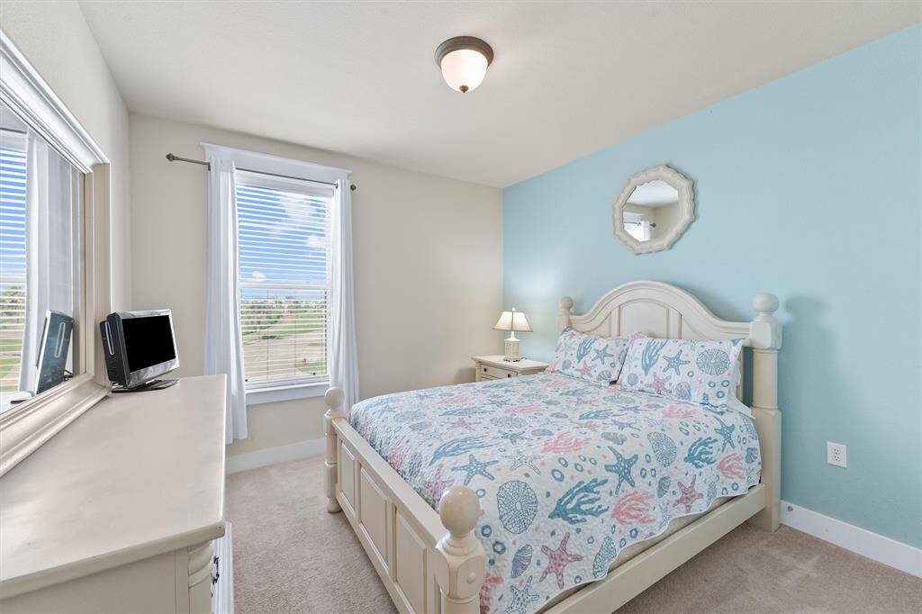 This guest bedroom features a charming coastal-themed decor with a King-sized bed adorned with sea-inspired bedding. The room is brightened by natural light from two large windows with white curtains, offering a serene view outside.