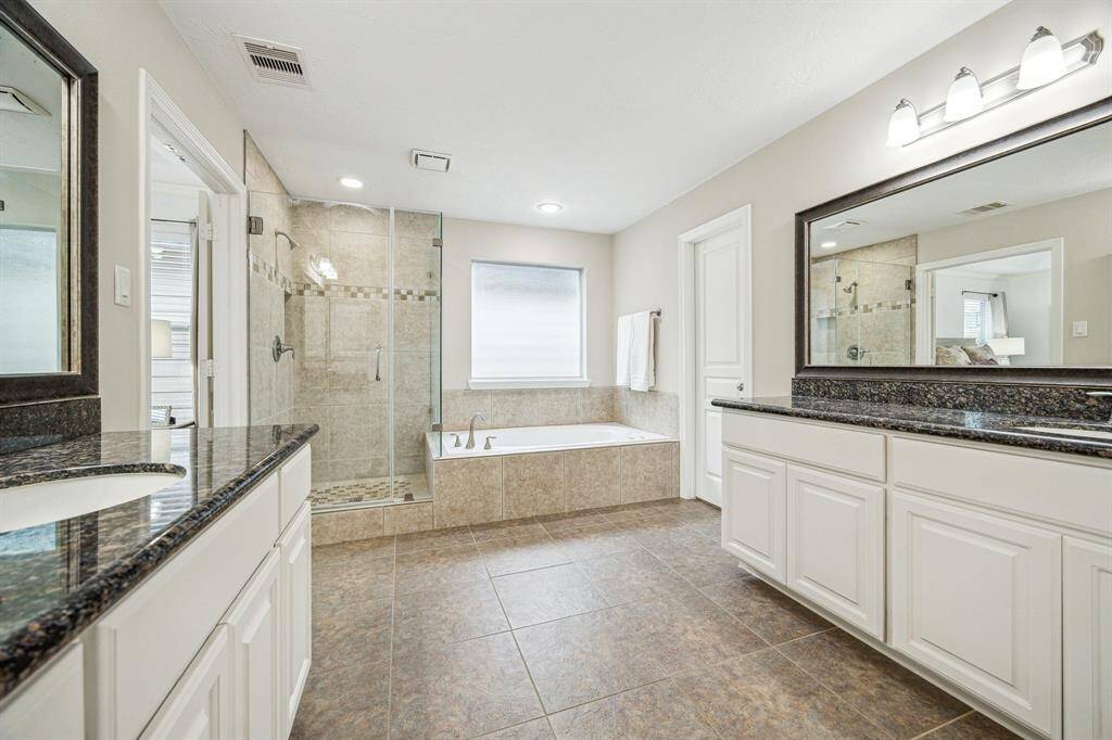 Primary bathroom with tile floors, recessed and sconce lighting, and granite countertops.