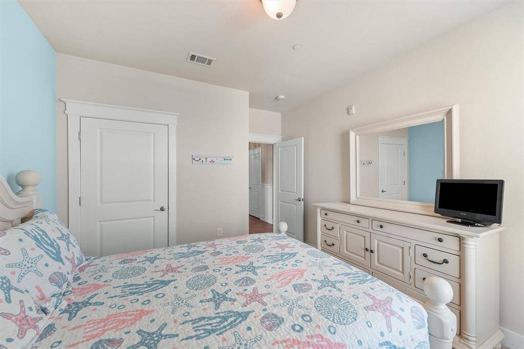 This view of the guest bedroom showcases the entrance to the room and the white dresser with a mirror. The decor maintains a consistent coastal theme, with pastel colors and sea-inspired patterns on the bedding, providing a calm and cozy environment for guests.