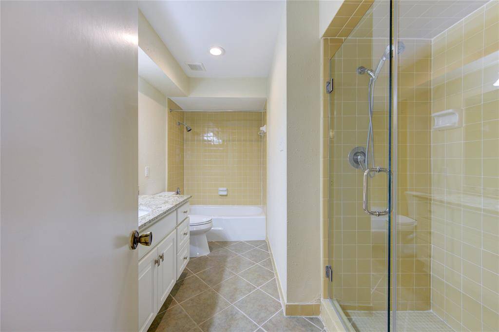 Spacious Primary bathroom with a glass-enclosed shower, and tub. Features light yellow tiles and modern fixtures, creating a bright and inviting space.
