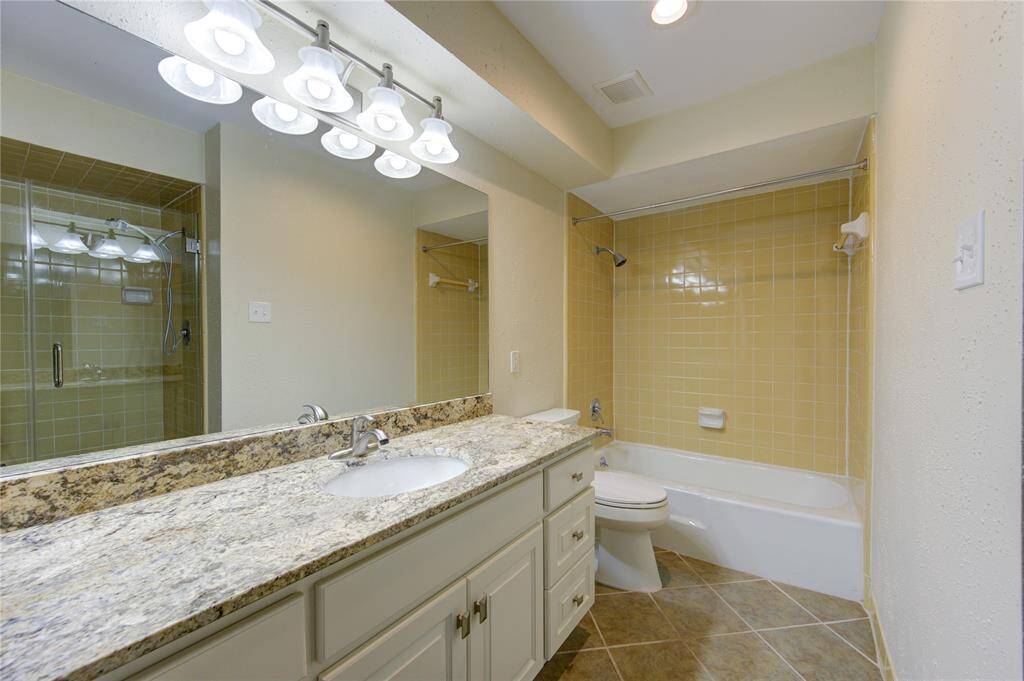 This bathroom features a granite countertop with a single sink, under-cabinet storage, and a well-lit vanity. It includes a shower-tub combo with tile floor.