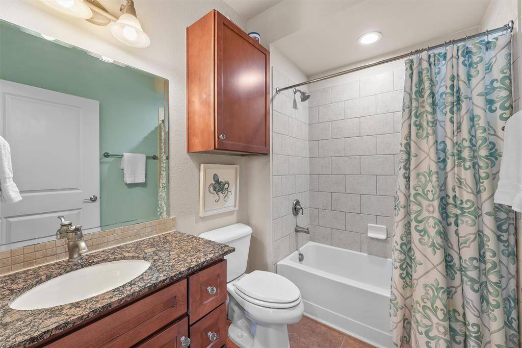 The guest bathroom is elegantly designed with a granite countertop and ample cabinet storage. The shower-tub combination features clean, modern tile work, complemented by a stylish shower curtain, creating a comfortable and inviting space for guests.
