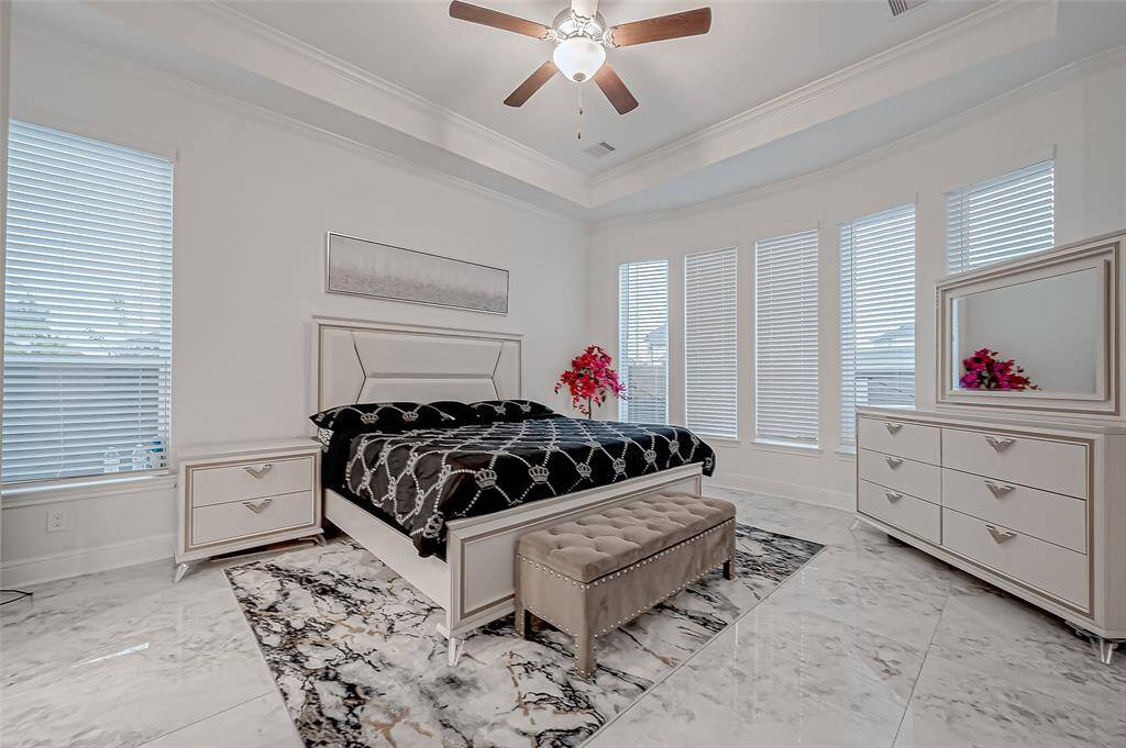 Two Lavish Primary Suites on the Main Level. Pictured is the First Primary Suite: Curved wall of windows for abundant natural light, tile marbled flooring and Tray ceiling.