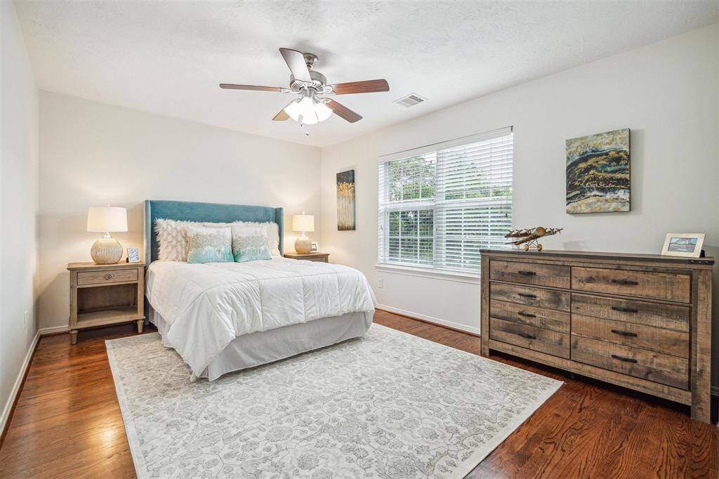 Third-floor secondary bedroom with hardwood floors, ceiling fan with lights, large window with blinds, and is en suite.