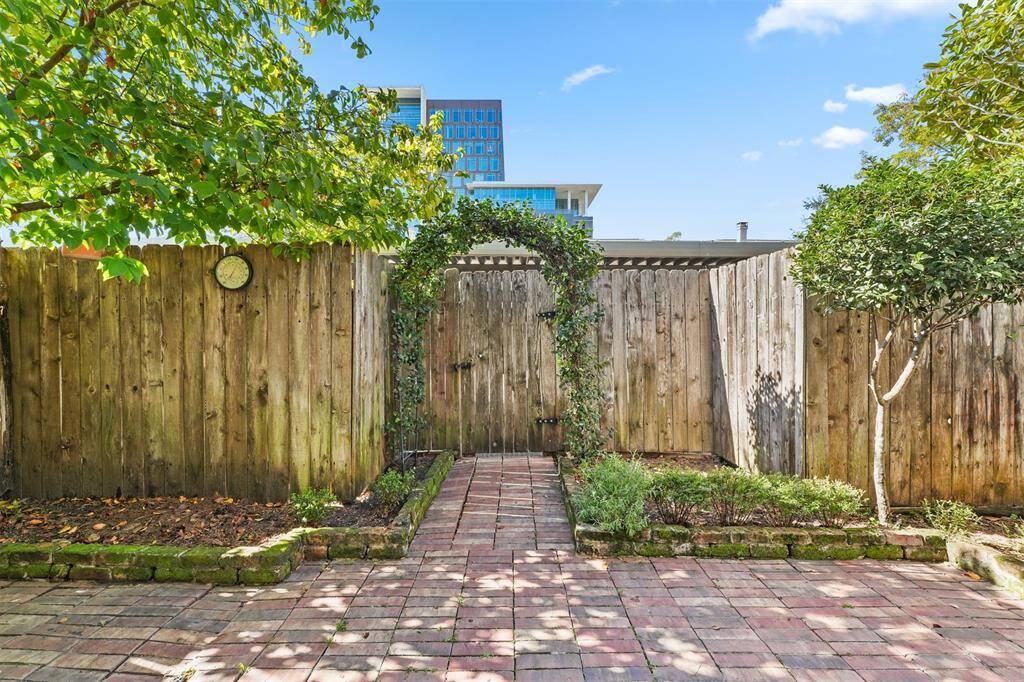 Charming backyard with a brick patio, surrounded by a wooden fence. Features a vine-covered archway and lush greenery, offering a cozy and private outdoor space.
