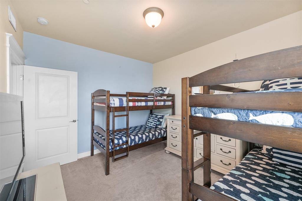Another view of the third bedroom showcases the arrangement of the wooden bunk beds and the blue accent wall. The room is furnished with a white dresser, maintaining the beach-themed decor with a relaxed, welcoming atmosphere.