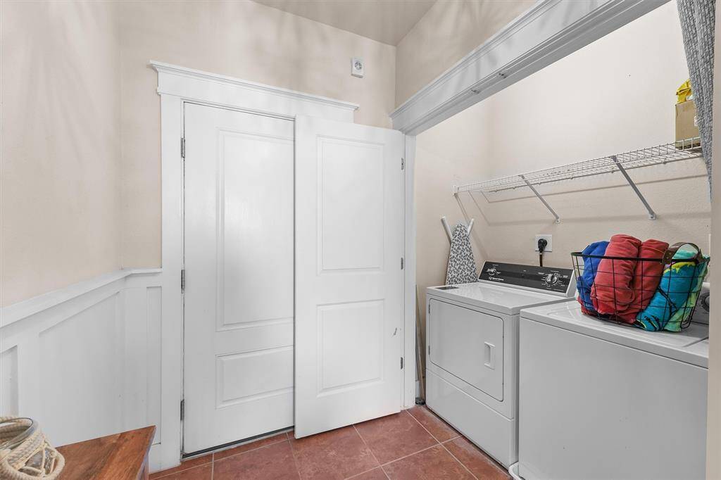 The laundry room is efficiently designed with a washer and dryer set, along with a convenient overhead shelf for storage. The space is well-organized, featuring double doors to maximize space and accessibility, making laundry tasks straightforward and manageable.