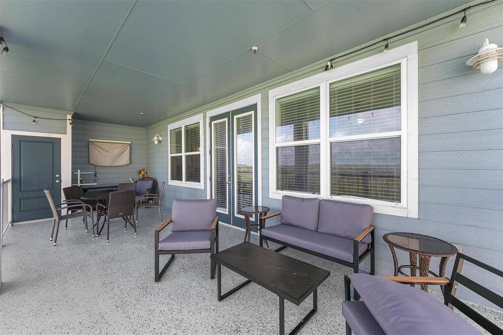 A wider view of the balcony reveals additional seating and a dining area, providing ample space for outdoor gatherings. The covered design ensures shade and protection, while the surrounding landscape adds a picturesque backdrop to this inviting outdoor space.