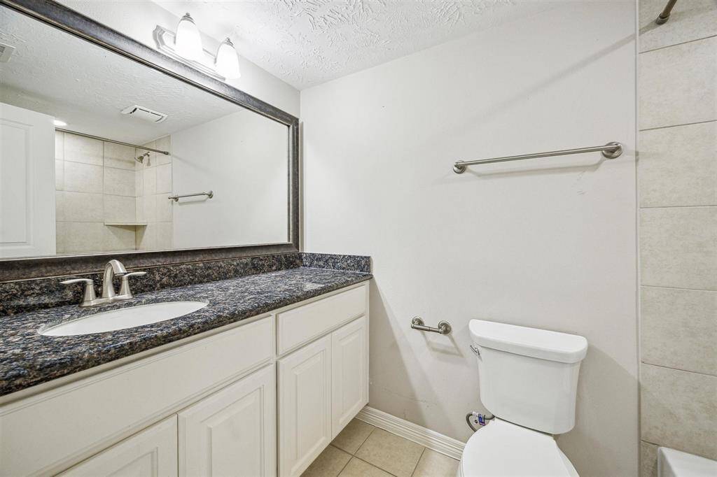 Secondary bathroom with tile floors, sconce lighting, granite counter top, and a tub/shower combo.