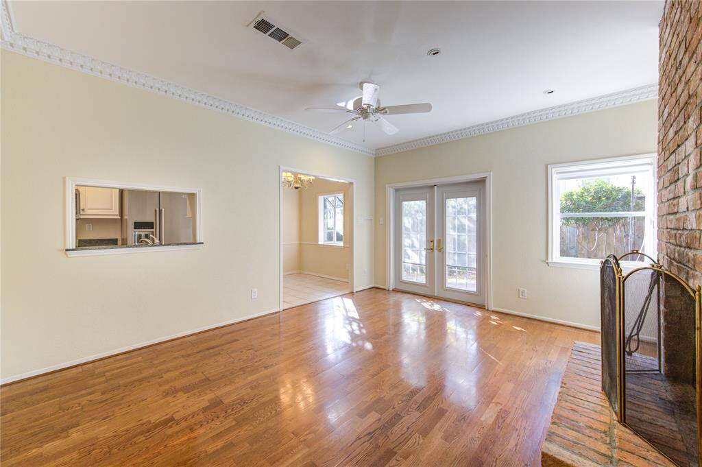 Bright family room with engineered wood floors, a ceiling fan, and a brick fireplace. Features French doors leading to the backyard and a passthrough window to the kitchen.