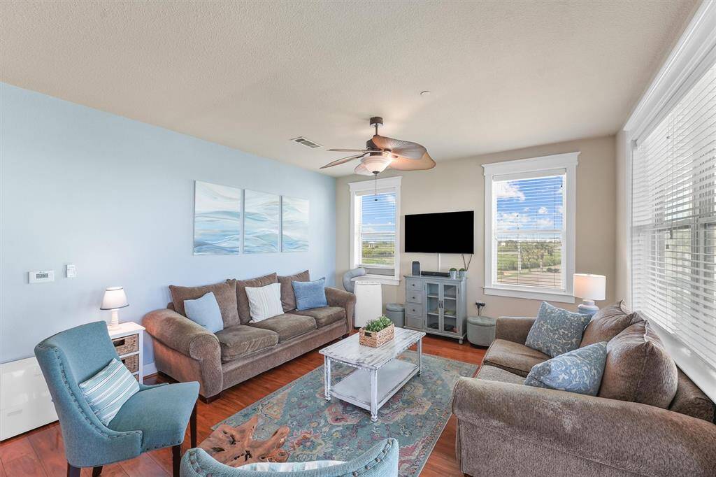 This angle of the living room highlights its spaciousness and natural lighting from multiple windows. The decor emphasizes a coastal theme with light blue accents and ocean-inspired artwork, making the room feel tranquil and welcoming.