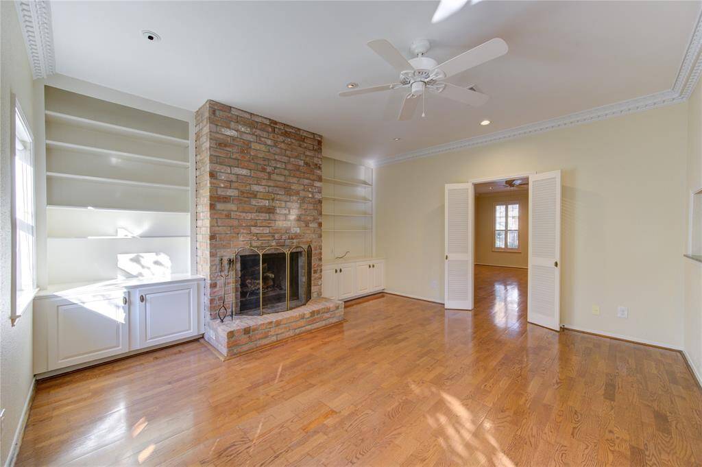 This cozy family room features a charming brick fireplace flanked by two built-in shelves, and ample natural light. It has warm engineered floors and a ceiling fan, with an inviting entryway leading to the formal dining room.