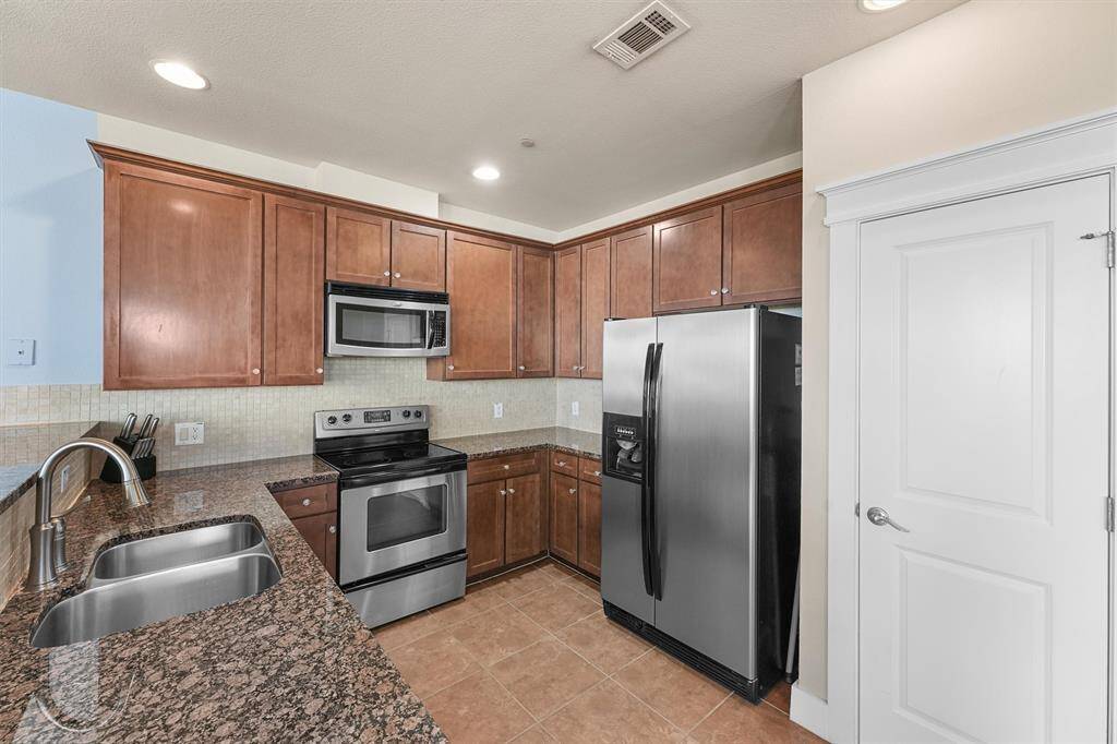 The kitchen is equipped with modern stainless steel appliances, including a microwave, oven, and refrigerator. The warm wood cabinetry offers plenty of storage, while the granite countertops provide a durable and stylish workspace.